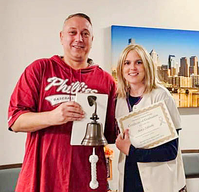 Stacy and husband with certificate and bell